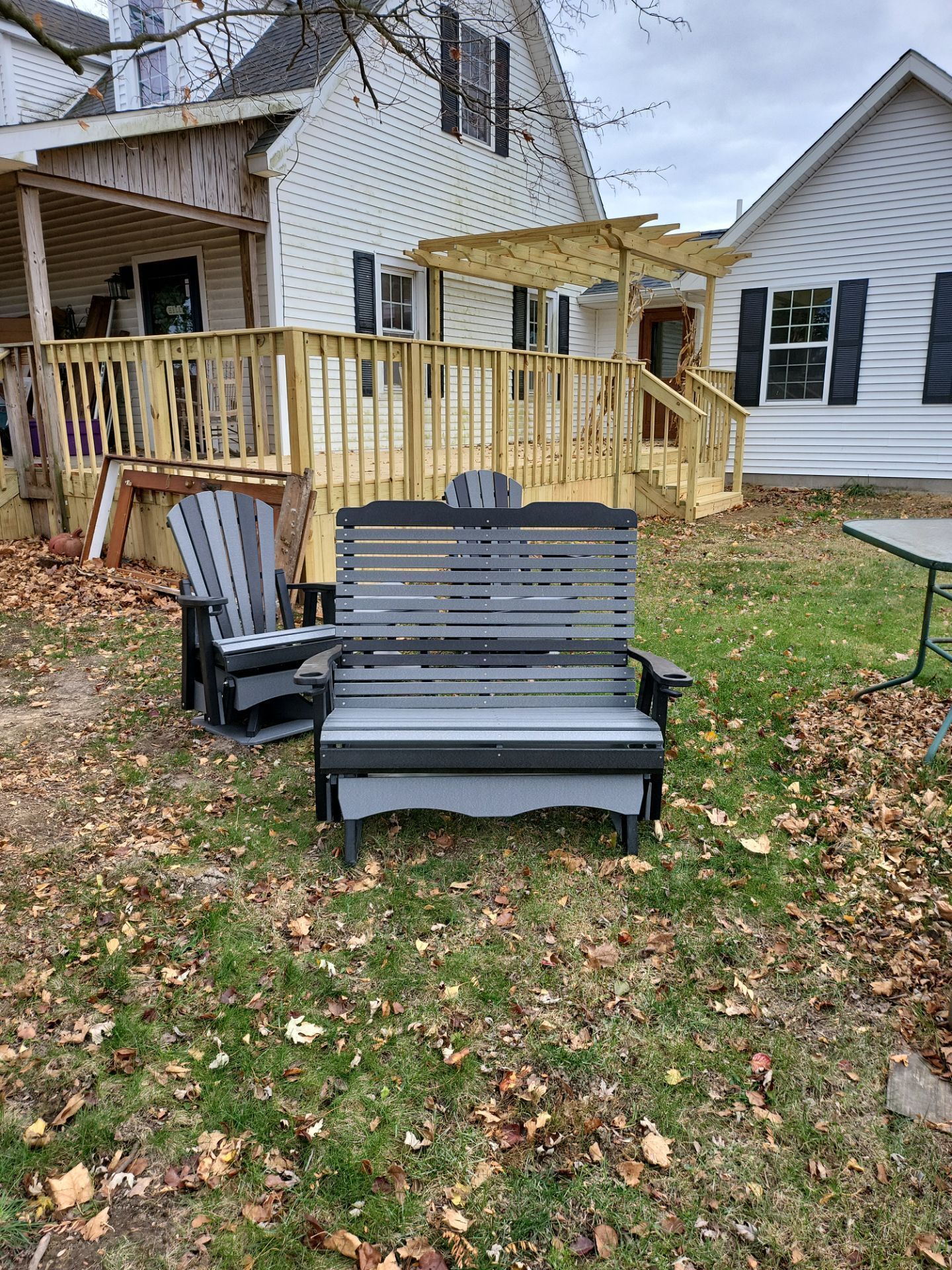 A swing and chairs are sitting in the grass in front of a house.