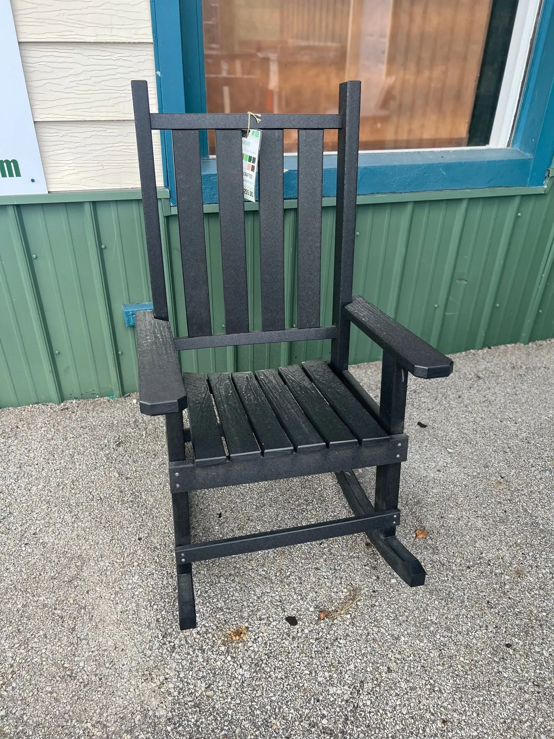 A black rocking chair is sitting in front of a green wall.