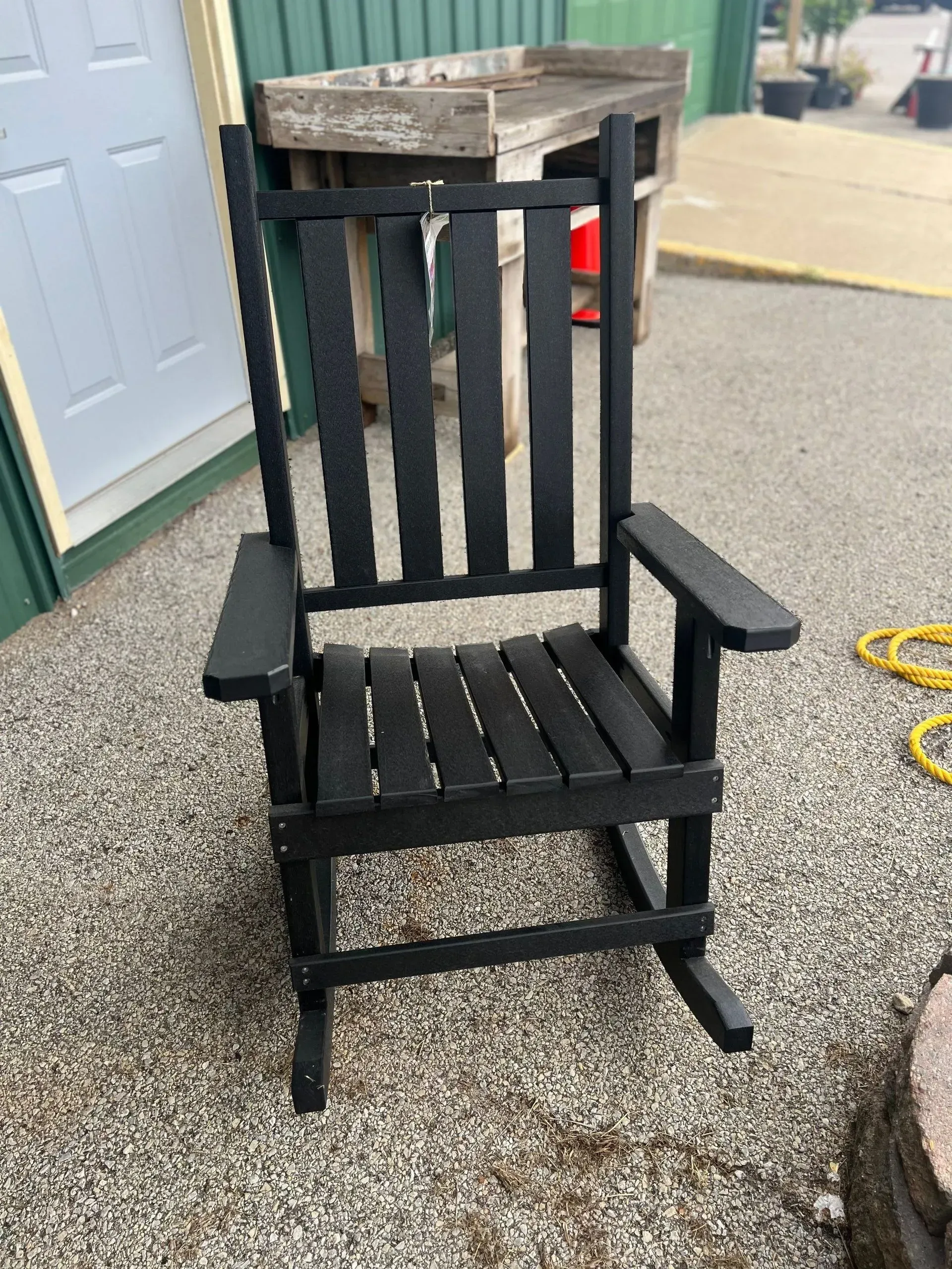 A black rocking chair is sitting on gravel in front of a building.