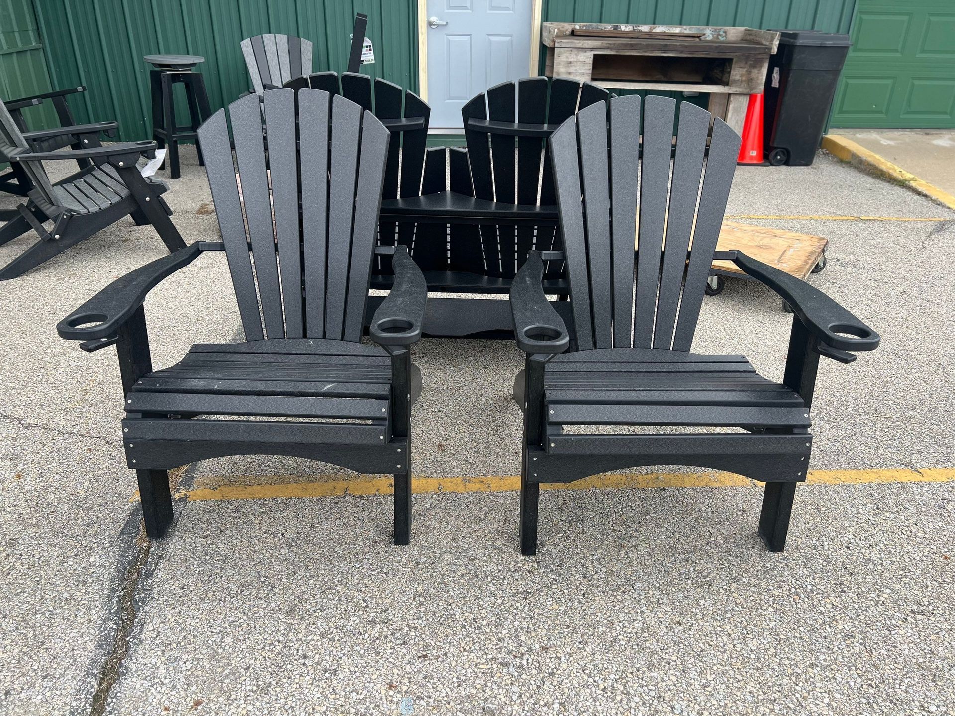 Two black adirondack chairs are sitting next to each other in a parking lot.