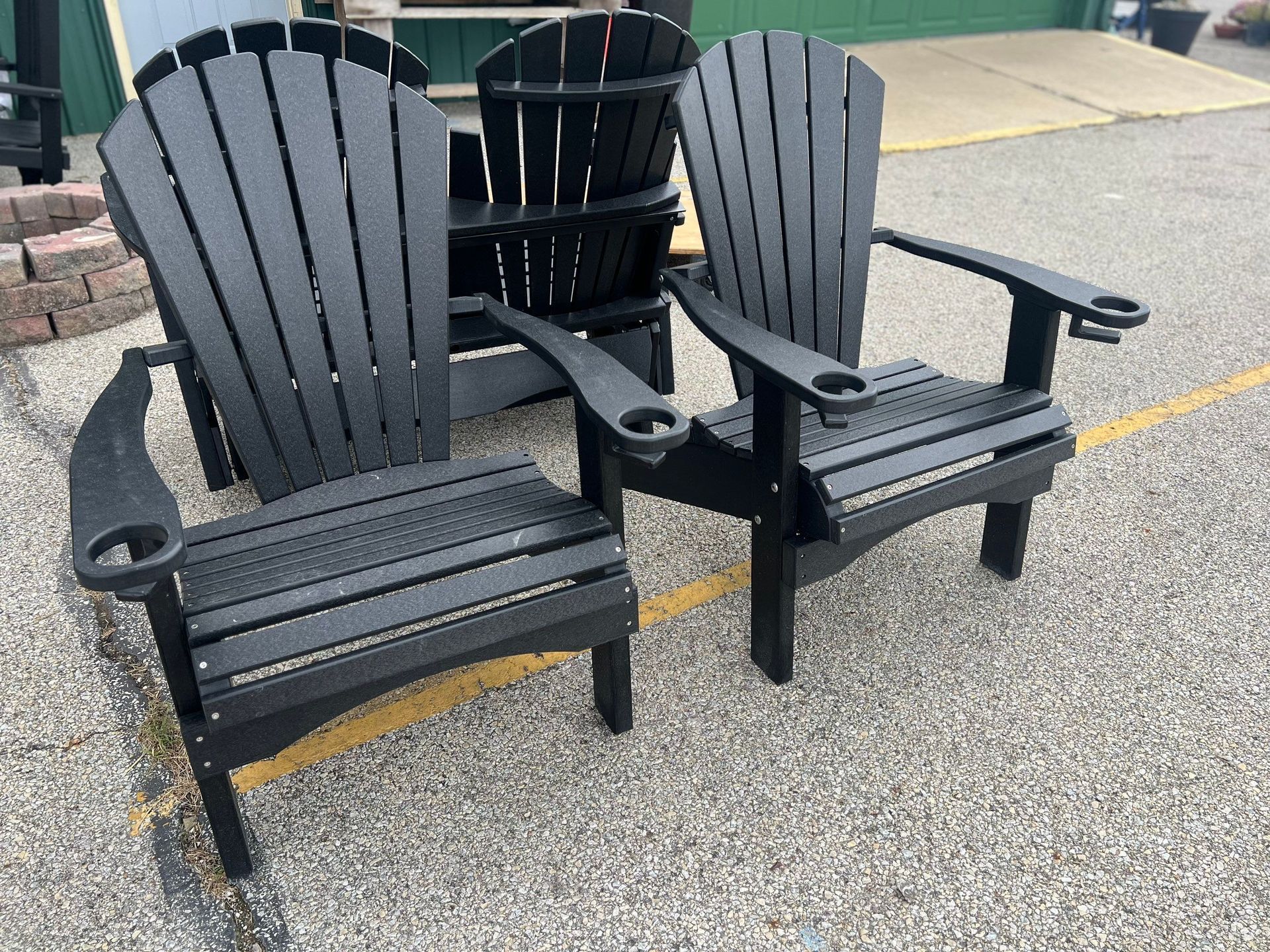 Three black adirondack chairs are sitting on a gravel road.
