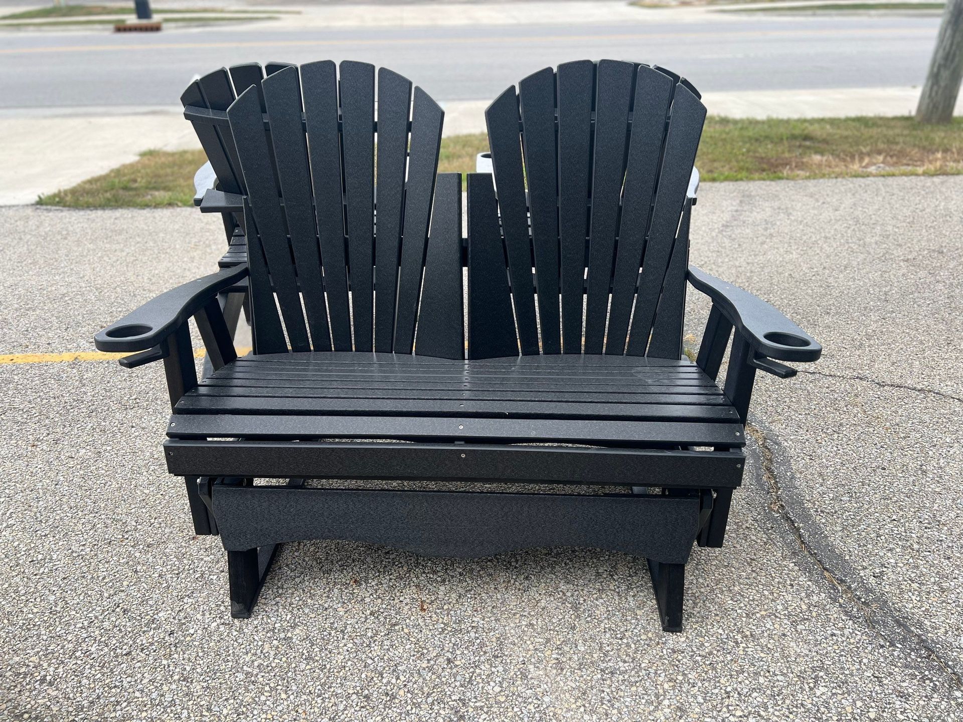 A black adirondack chair is sitting on the side of the road