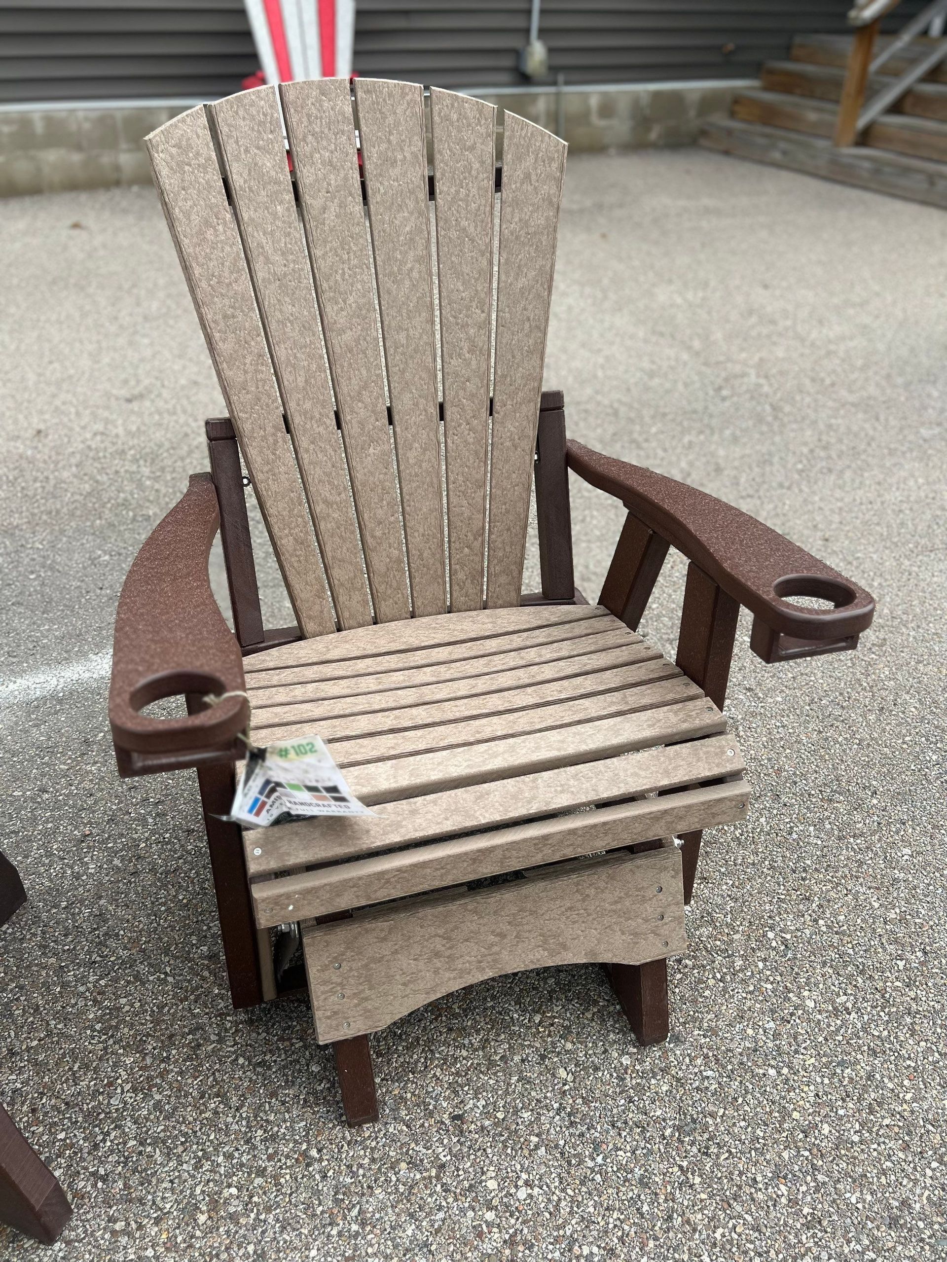 A wooden chair with a foot rest is sitting on a gravel road.