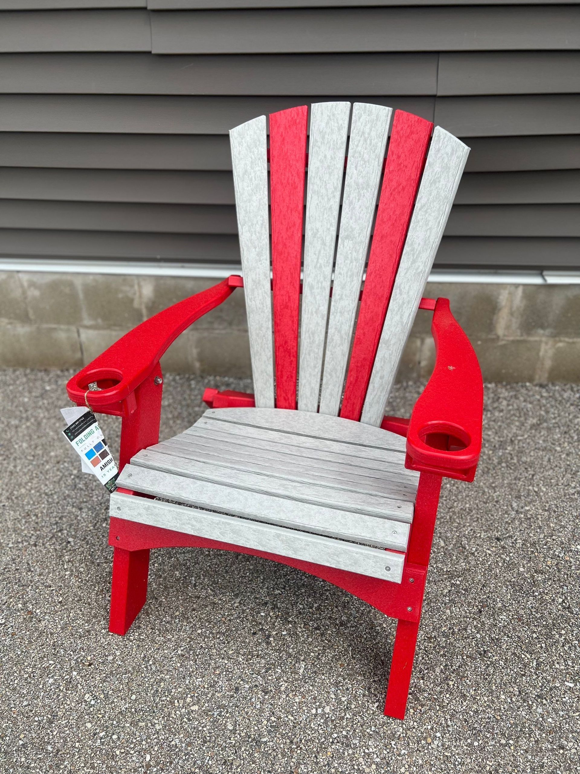 A red and white adirondack chair is sitting on gravel in front of a building.
