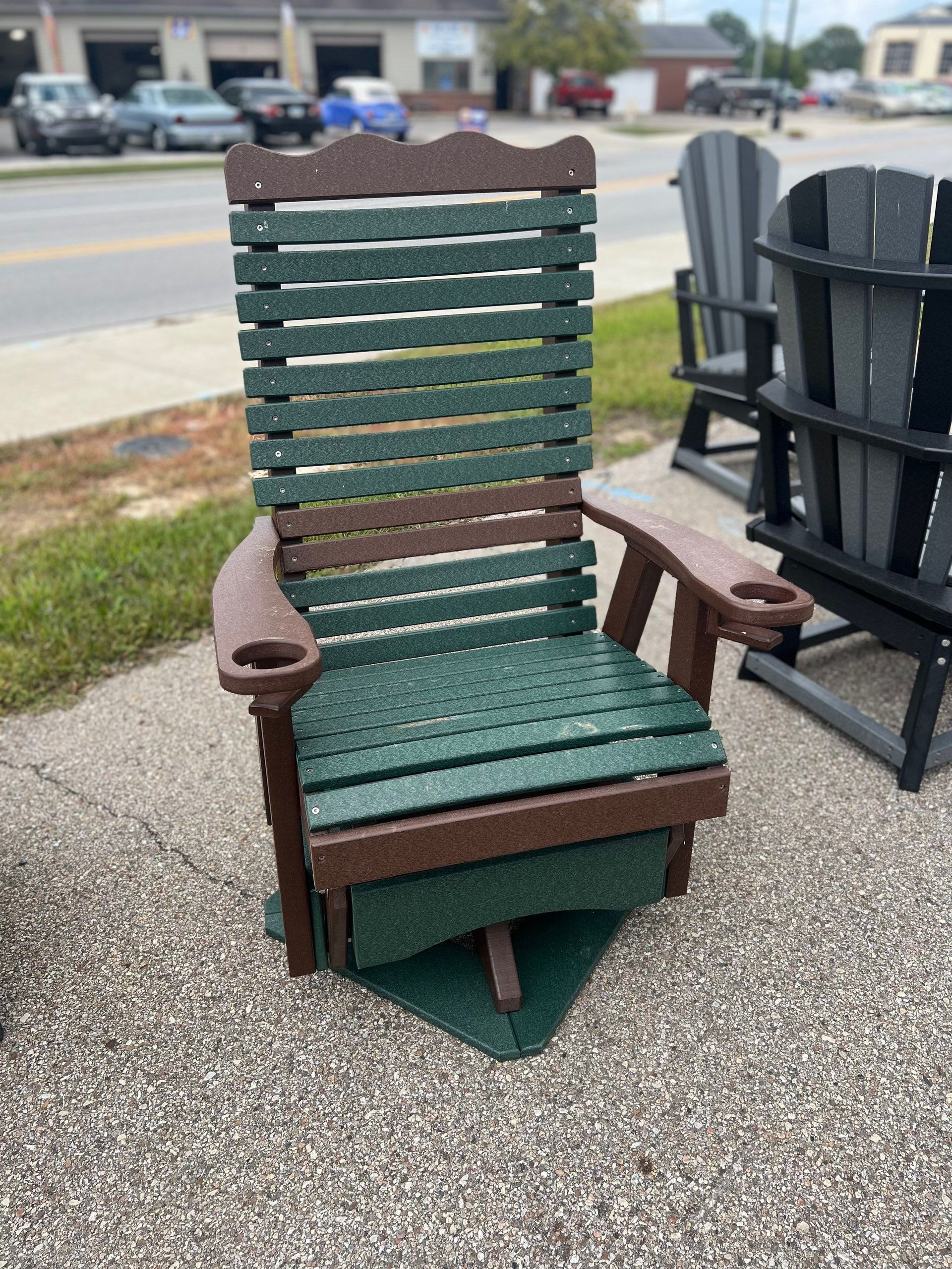 A green and brown wooden rocking chair is sitting on a sidewalk.
