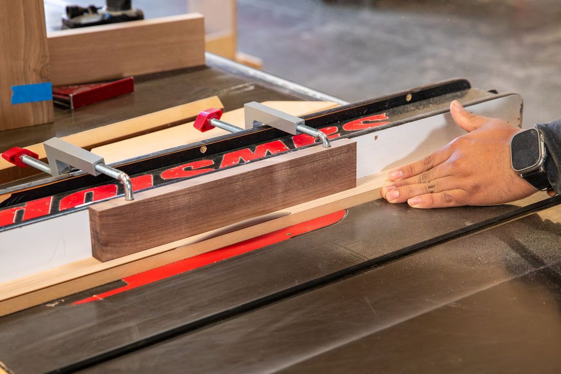 Person using a table saw to cut a wooden board. The board is clamped to a fence.