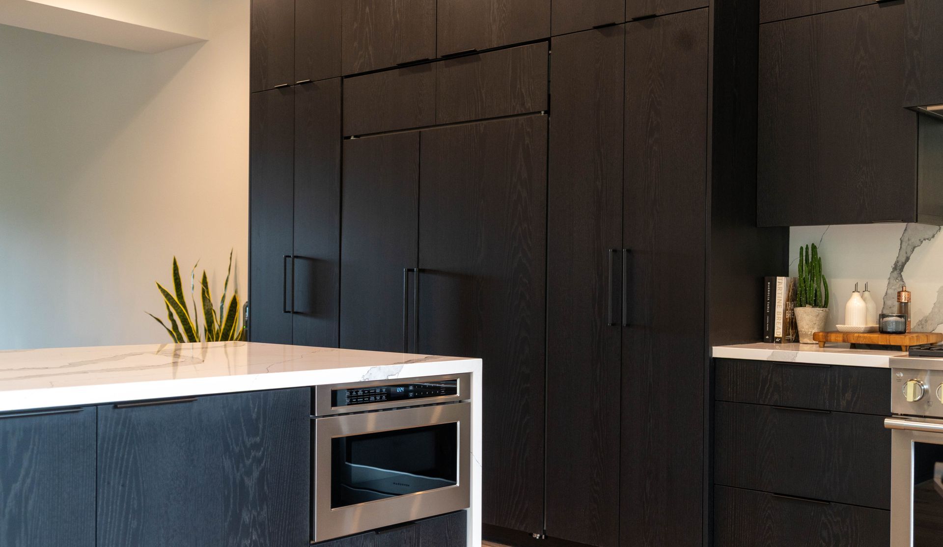 Modern kitchen with black cabinetry and white countertops. Stainless steel appliances.
