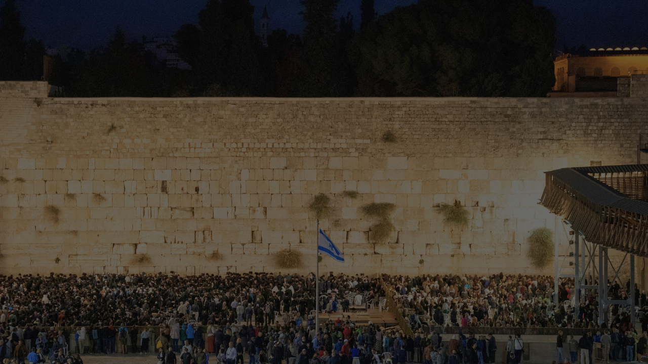Wide view of the Western Wall at night filled with people gathered in prayer in Jerusalem
