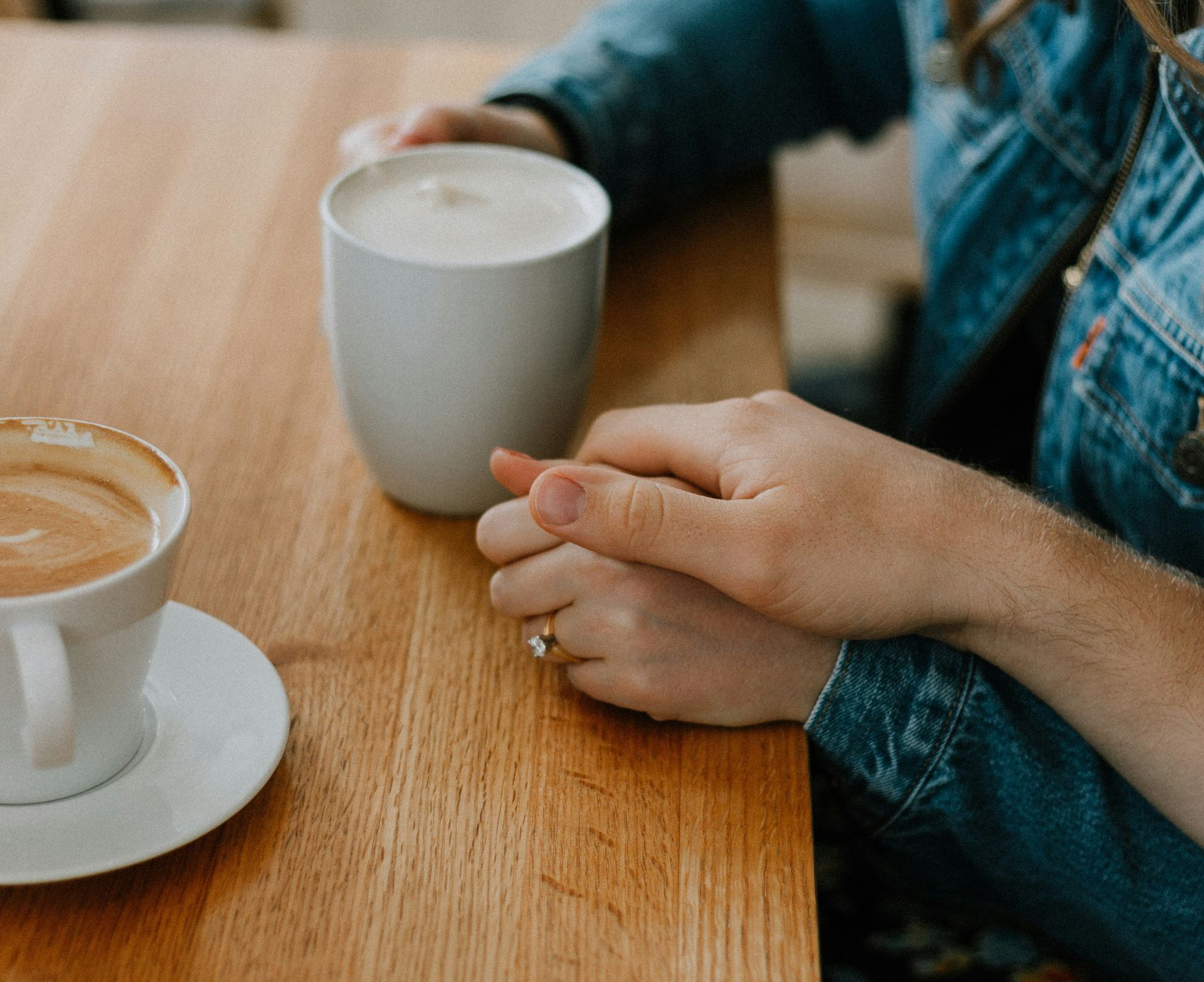 Close-up of two women holding hands in prayer and support over a latte at a table
