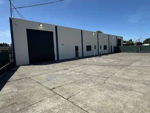 Exterior view of a commercial building with a large loading door and parking lot on a sunny day.