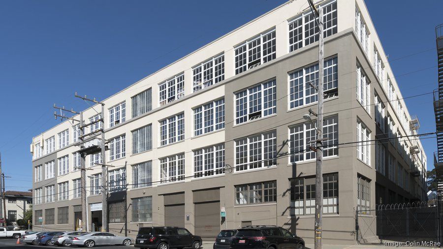 Multi-story building, exterior view. Light-colored facade with many windows and cars parked in front.