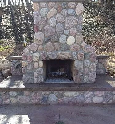Stone outdoor fireplace with a large chimney and built-in hearth on a patio.