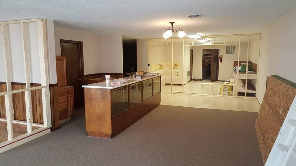 Empty living room with beige carpet, wooden counter, and kitchen area in the background
