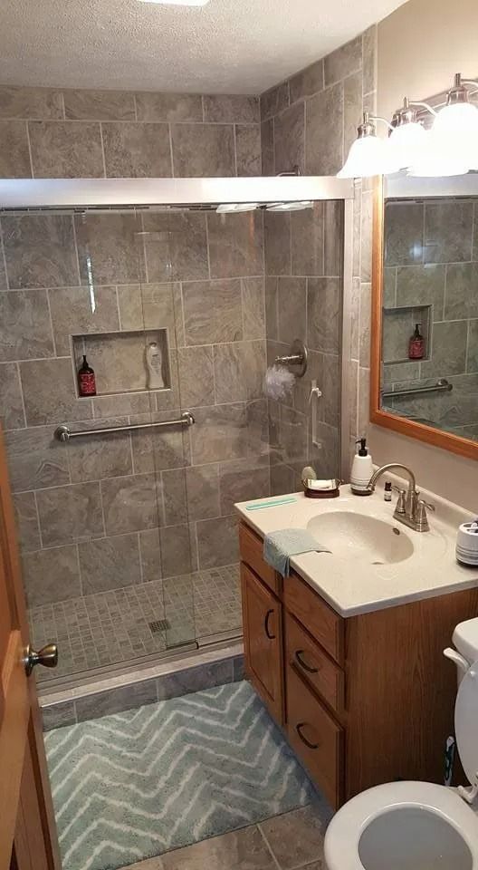 Small tiled bathroom with shower, sink vanity, mirror, and striped bath mat.
