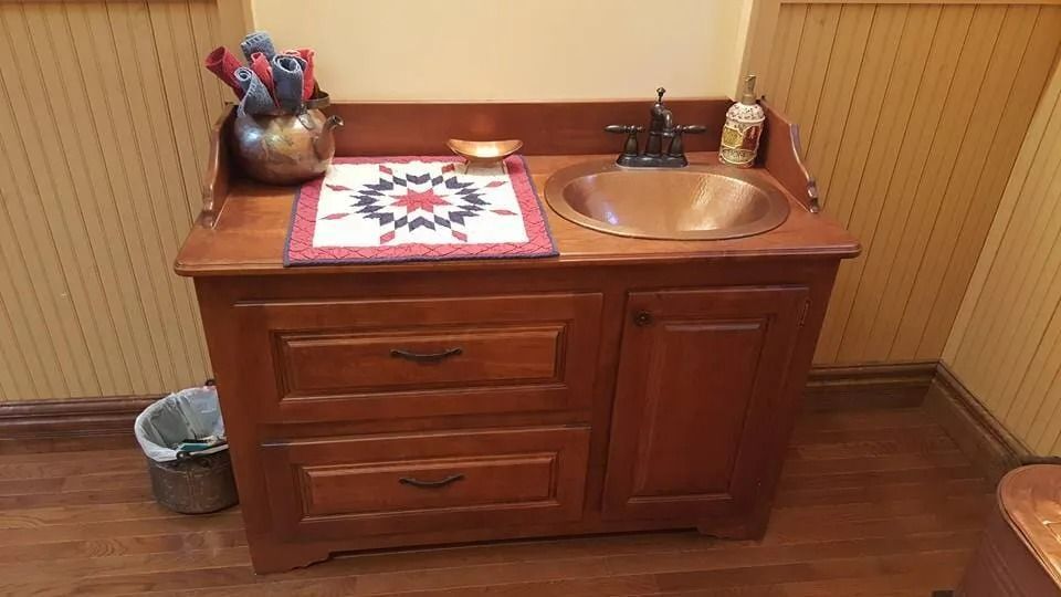 Wooden bathroom vanity with drawers, copper sink, and toiletries in a warm wood-paneled room