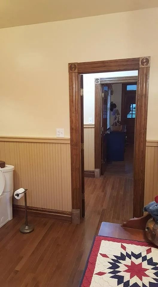 Wood-paneled hallway with an open doorway, hardwood floor, and a patterned rug in the foreground