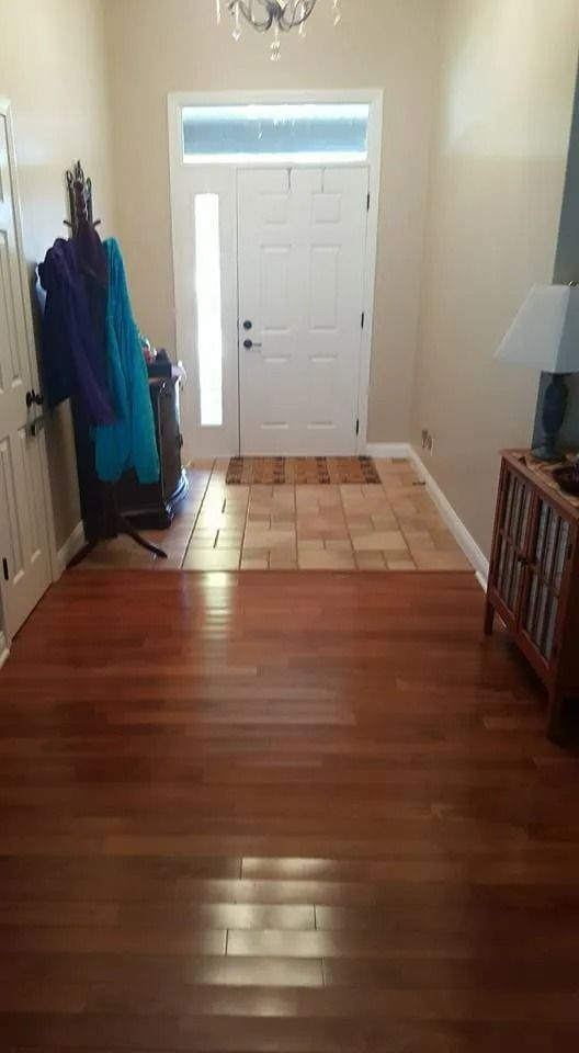 Hallway with hardwood floor, rug by the front door, coat rack on the left, and a white entry door ahead.