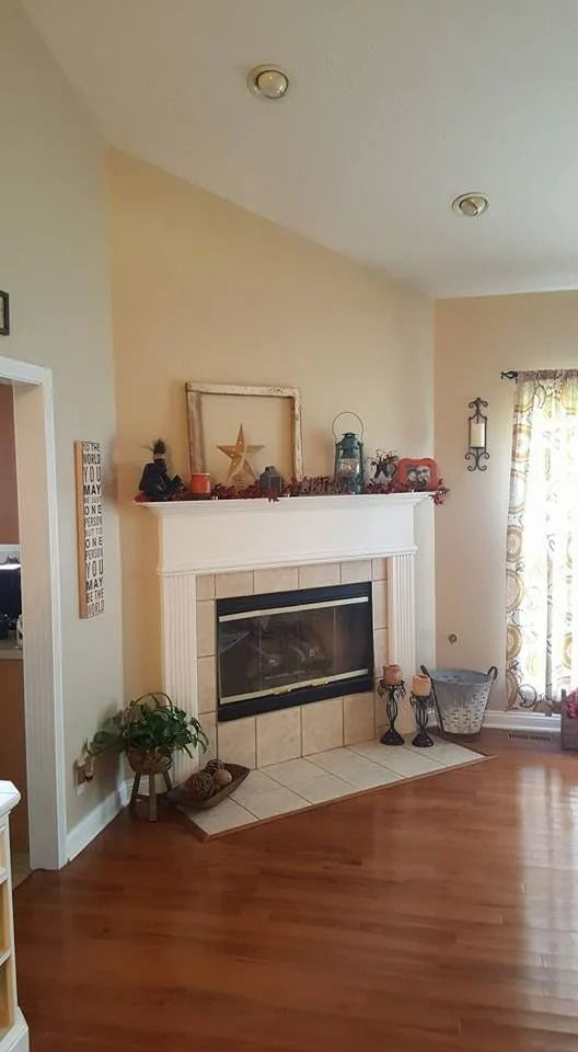 Living room with white fireplace, wooden floor, and tall window with curtains