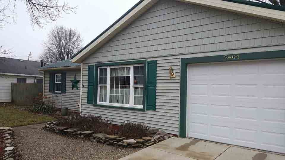 Suburban house exterior with white siding, green shutters, and a garage on a cloudy day