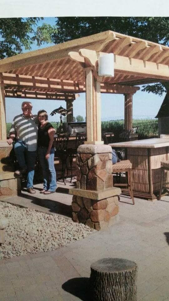 People standing under a wooden gazebo at an outdoor park or picnic area.