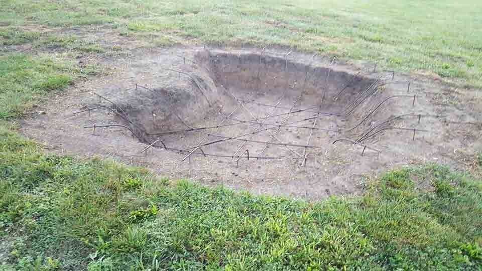 Large shallow dirt pit in a grassy field with cracked soil at the center