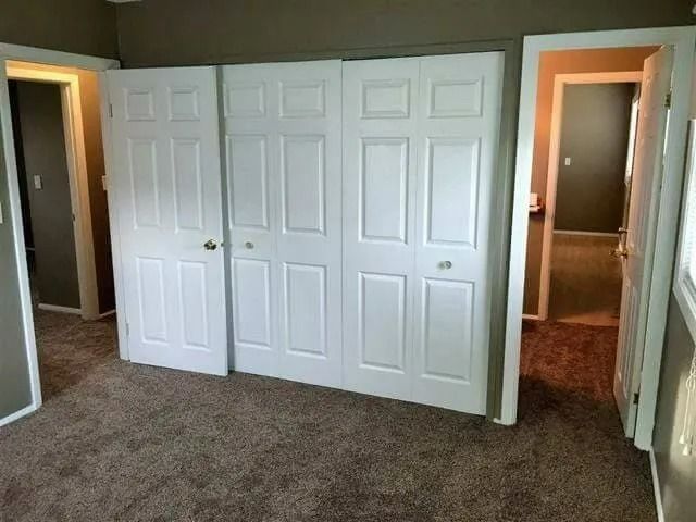 Bedroom with four white closet doors and carpeted floor, viewed from a doorway