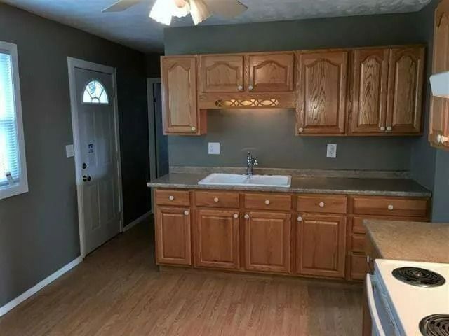 Empty kitchen with wood cabinets, gray walls, white sink, and laminate floor.