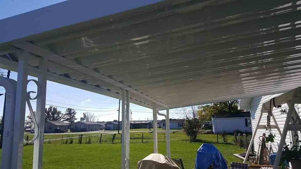 Covered patio overlooking a sunny backyard with grass, trees, and a small shed in the distance