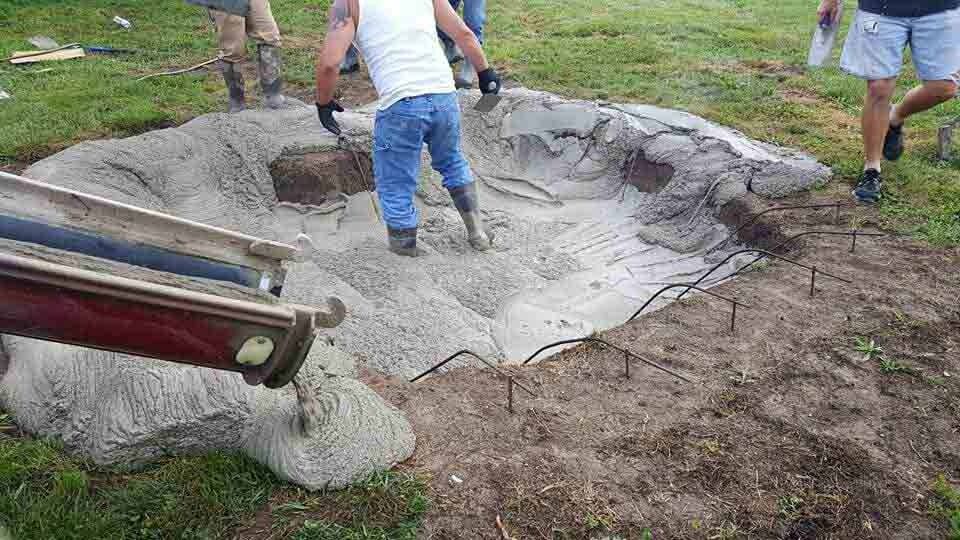 Workers around a large excavated pit, using a tarp or liner in a grassy yard