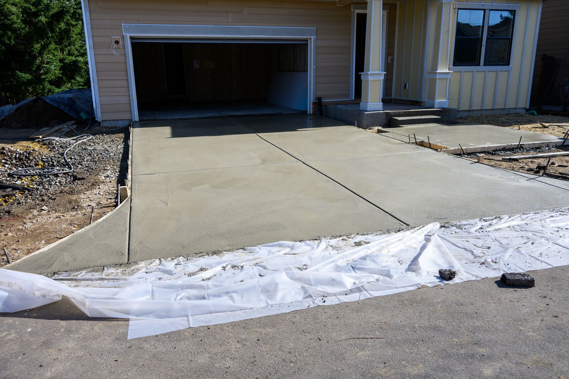Concrete driveway leading to an open garage with white silt fence at the curb in front