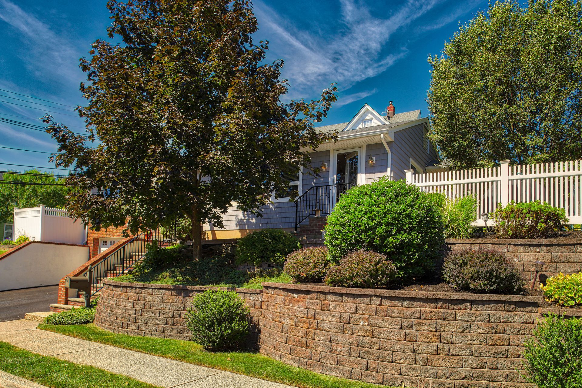 House with a front porch and landscaped yard behind a stone retaining wall under a blue sky