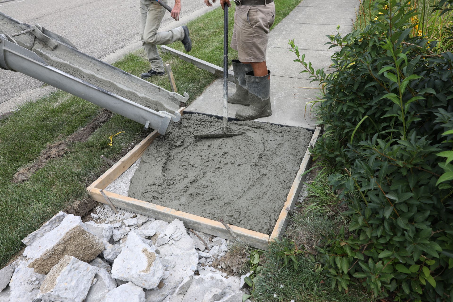 Worker smoothing wet concrete in a wooden form beside a walkway and garden plants
