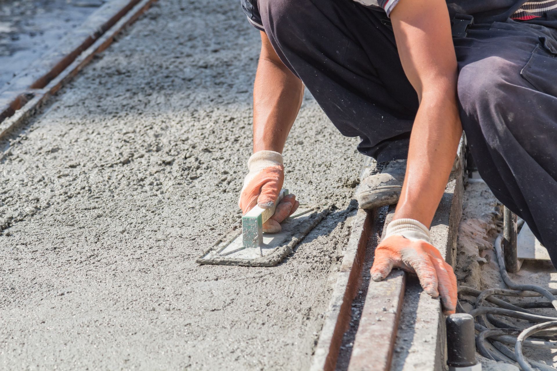 Worker smoothing wet concrete beside railroad tracks with a trowel