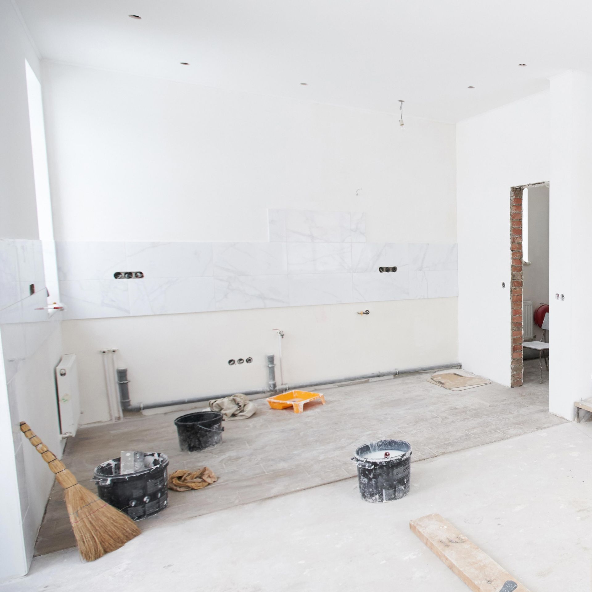 Unfinished white kitchen under renovation with tools, buckets, and tiled backsplash installed on the wall