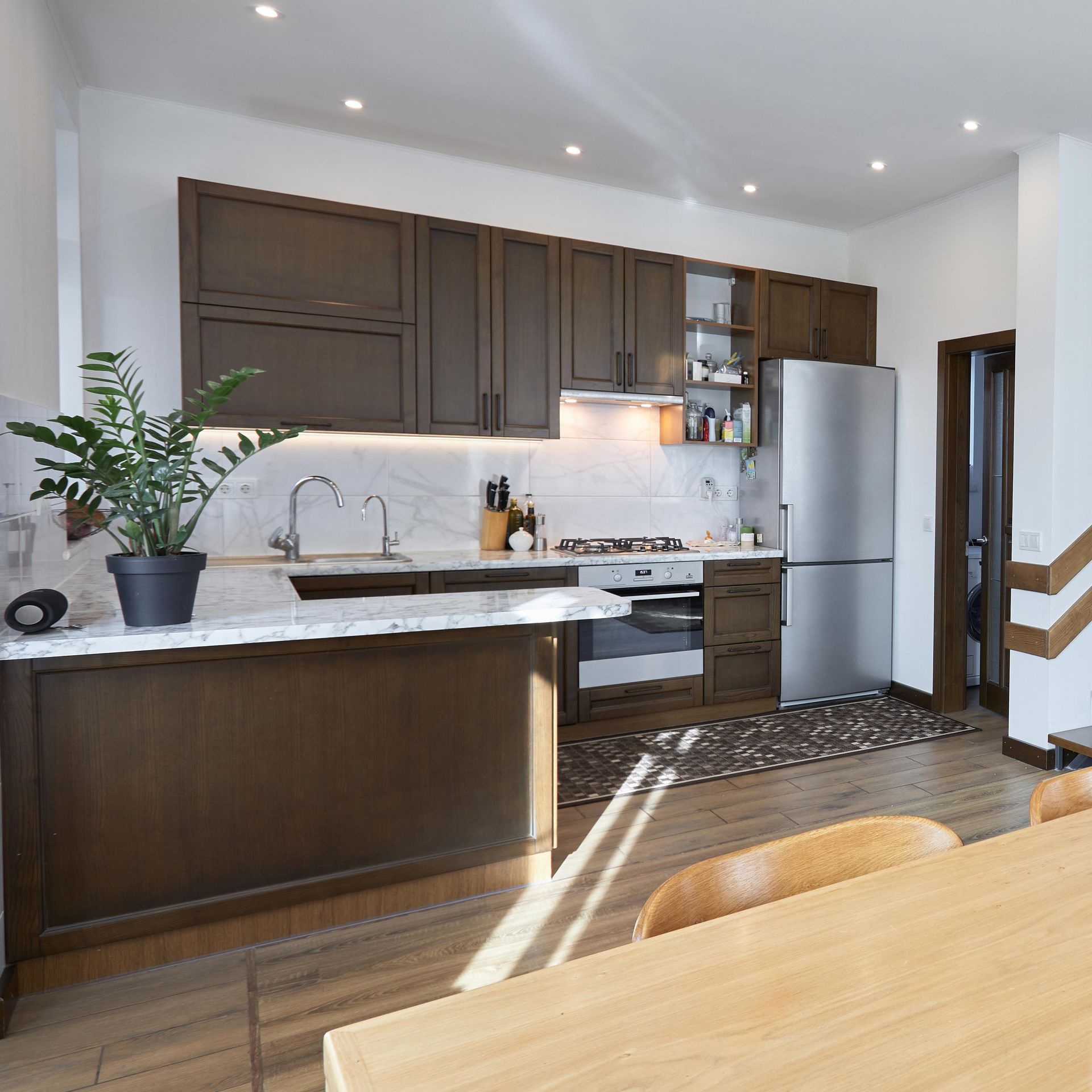 Modern kitchen with dark cabinets, stainless appliances, marble island, and a plant by the sink