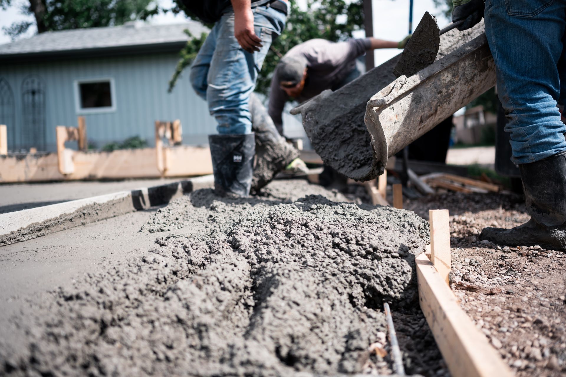 Workers pouring wet concrete into a wooden form at a construction site
