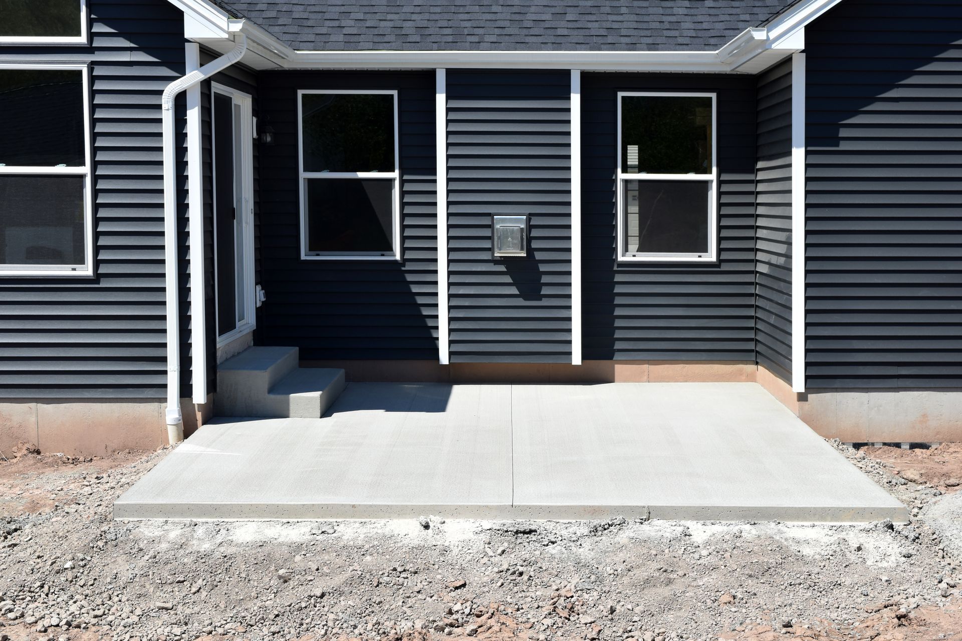 Front entrance of a dark gray house with a concrete patio and two windows.