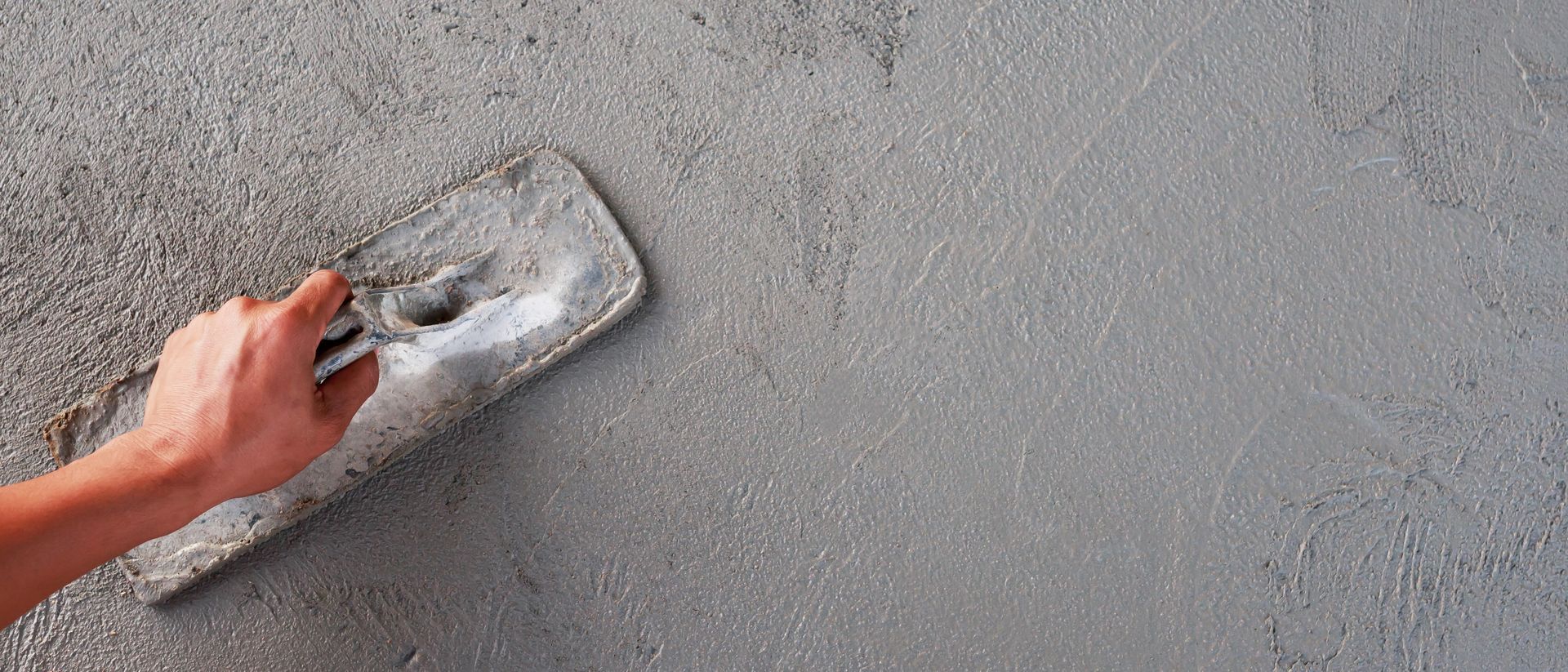 Hand smoothing a gray cement surface with a metal trowel.