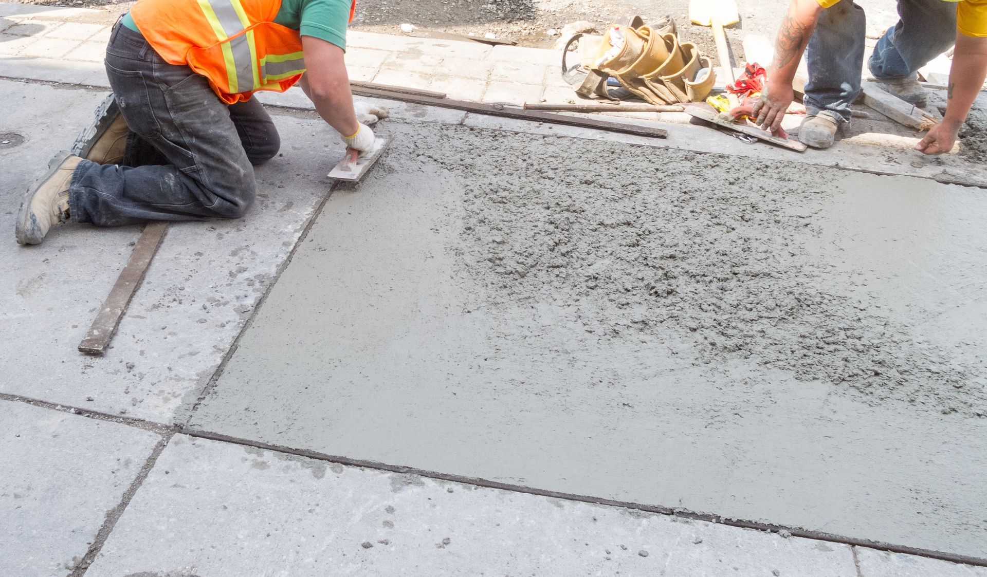 Workers smoothing wet concrete on a sidewalk at a construction site