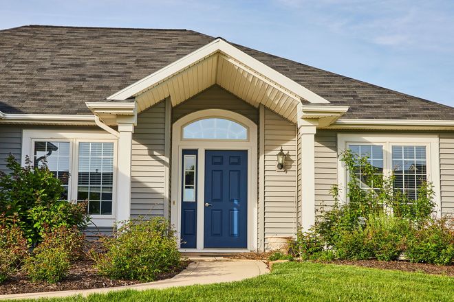 Front view of a house with blue front door, white siding, and landscaped shrubs under a gabled roof