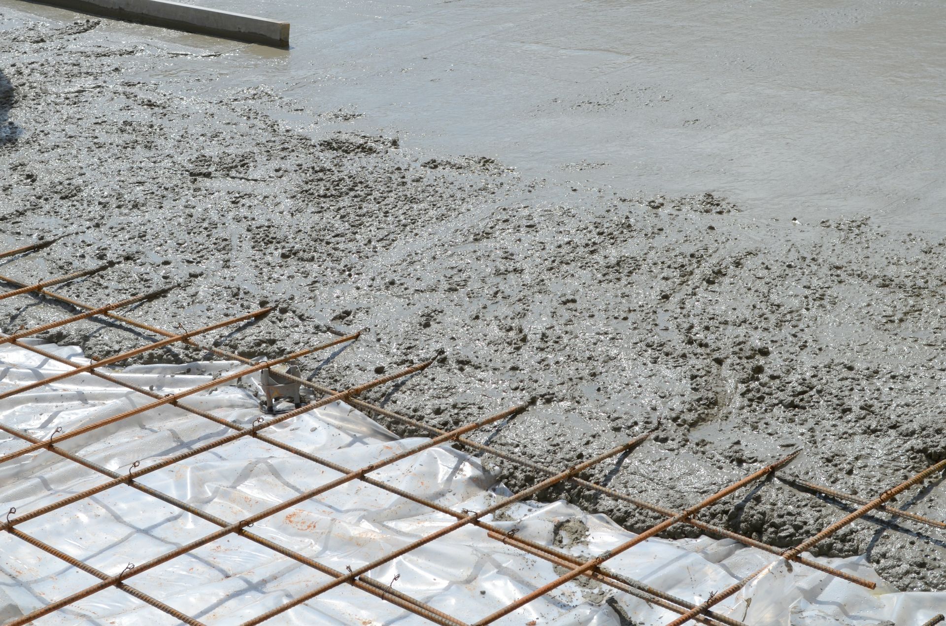 Wet concrete being poured over rebar and plastic sheeting at a construction site