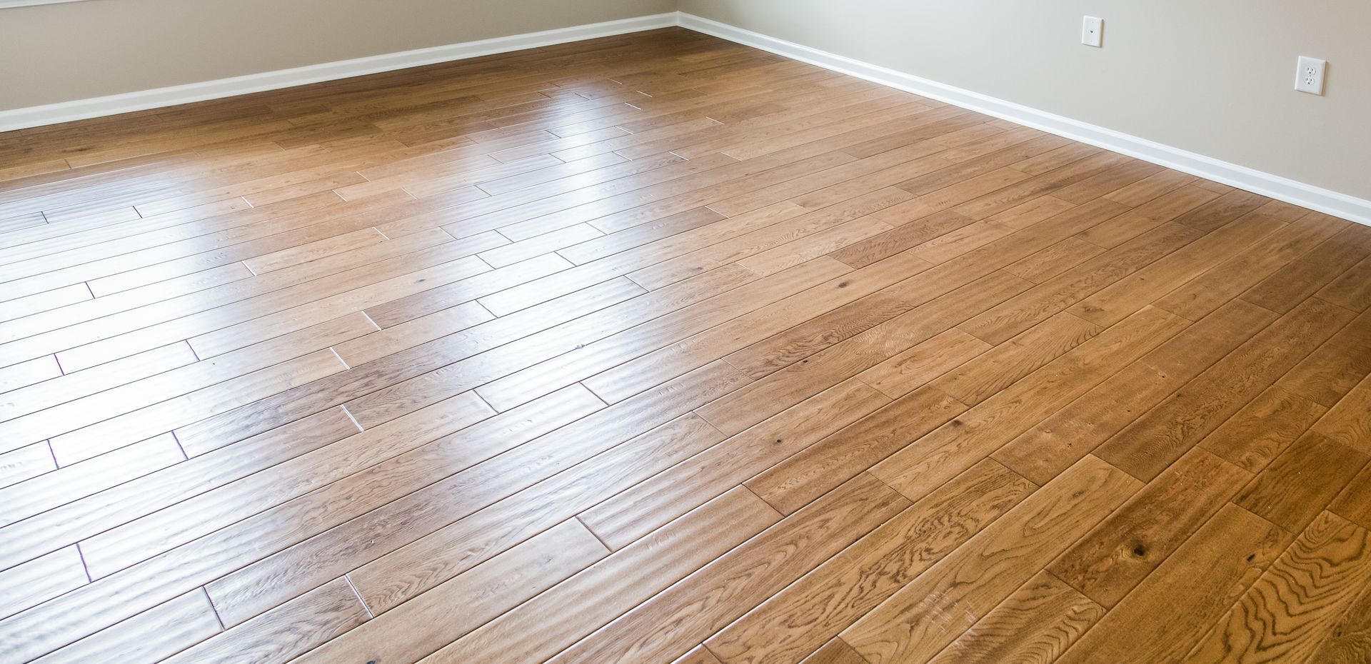 Empty hardwood floor in a sunlit room with light gray walls and white baseboards