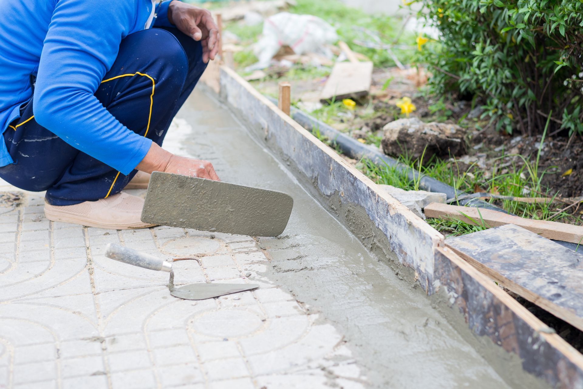 Person using a trowel to smooth wet concrete in a formwork, outdoors.