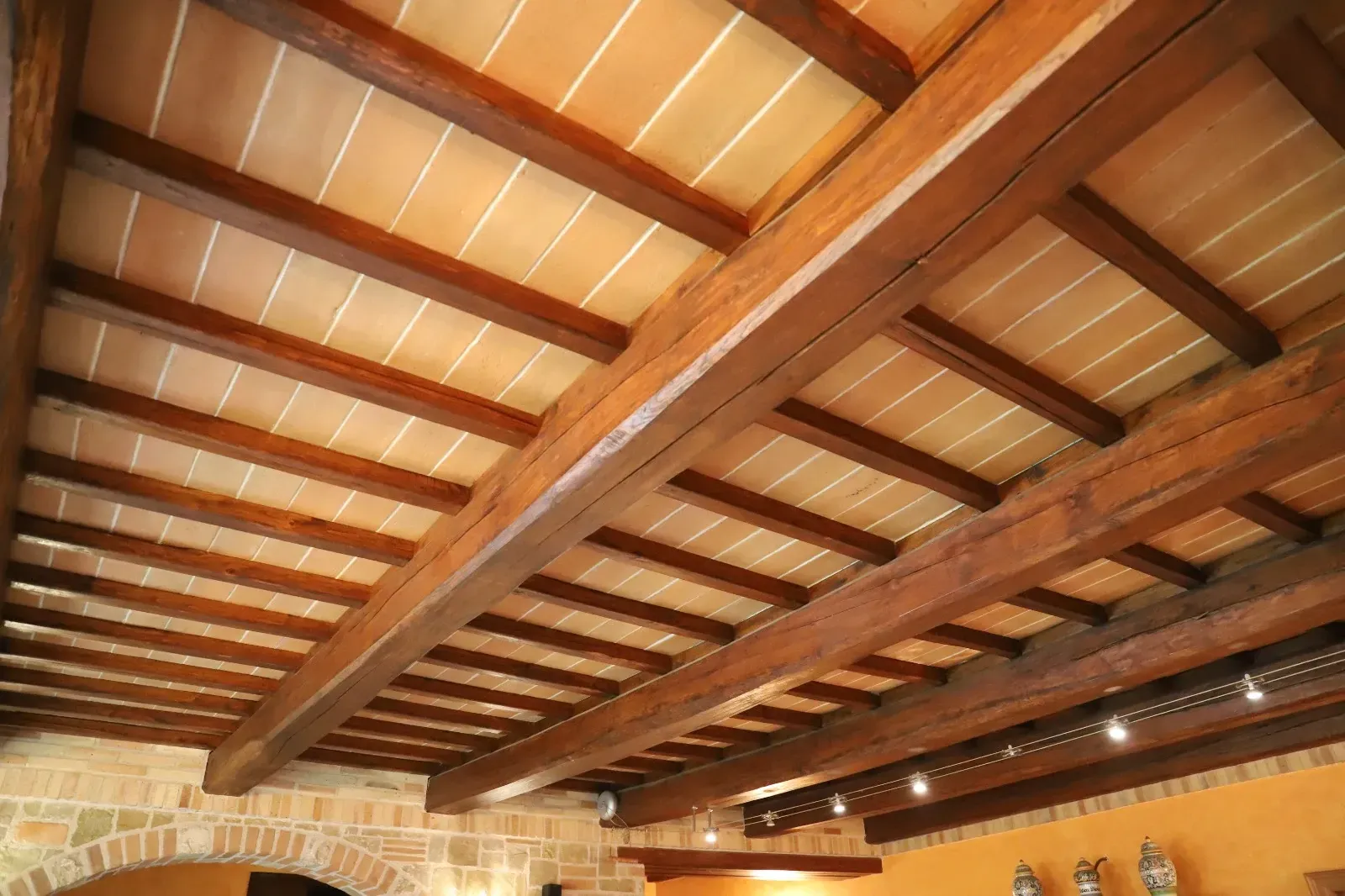 Soffitto con travi in legno, piastrelle in terracotta e pareti in pietra in un interno rustico.