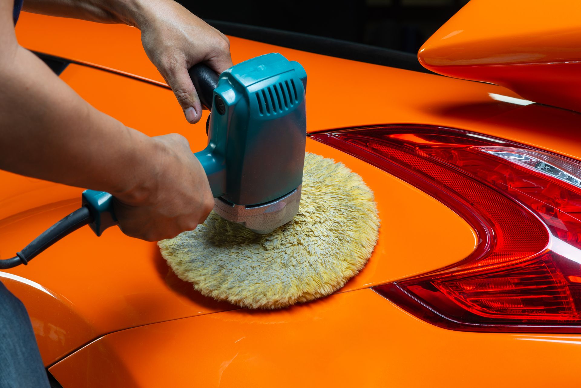 A person is polishing an orange car with a machine.