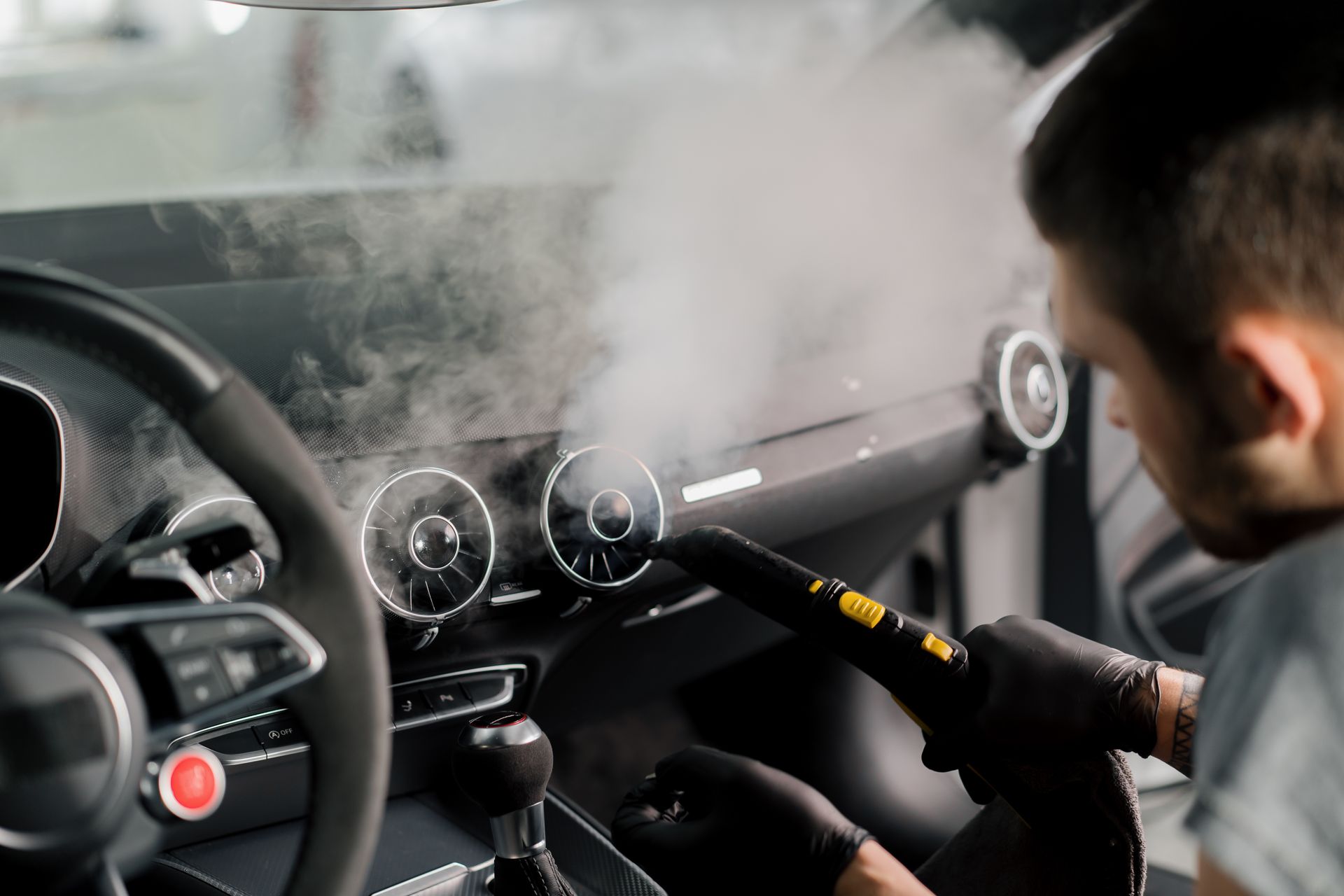A man is cleaning the interior of a car with a steam cleaner.