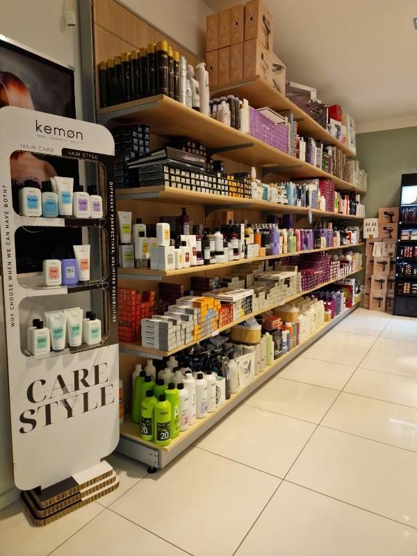 Uno scaffale di un salone di bellezza, rifornito di prodotti per la cura e lo styling dei capelli, in un corridoio luminoso del negozio.