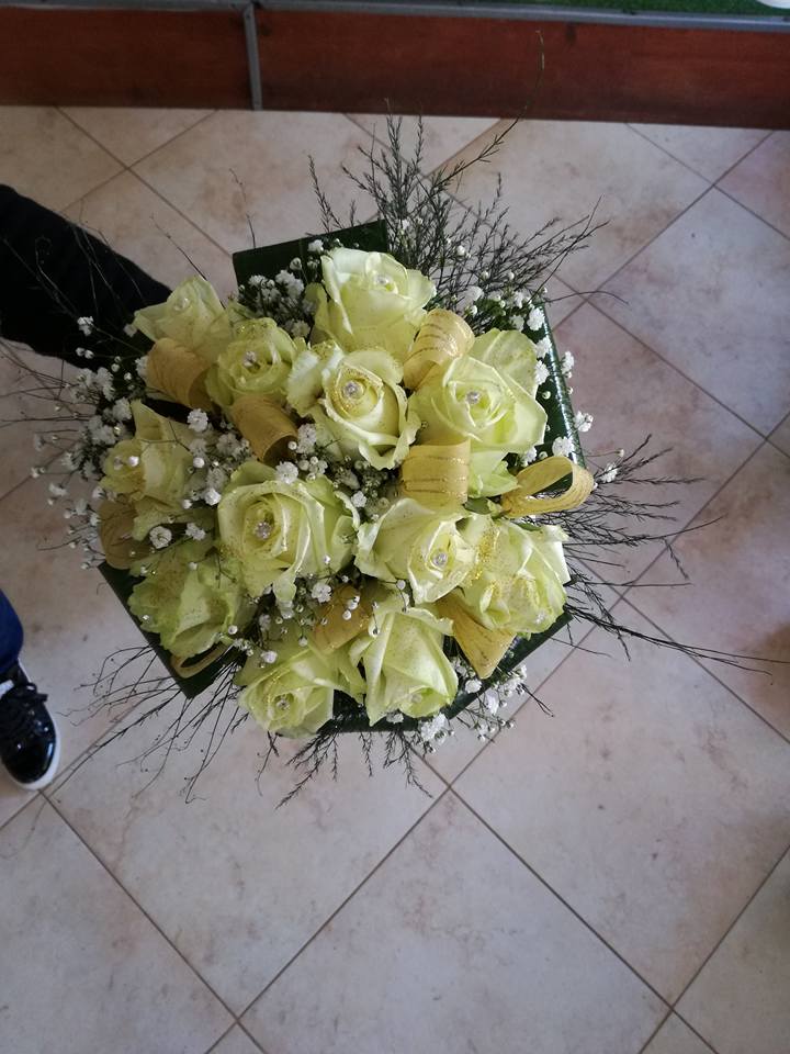Bouquet di rose giallo pallido con piccoli fiori bianchi, foglie verdi e nastro dorato.