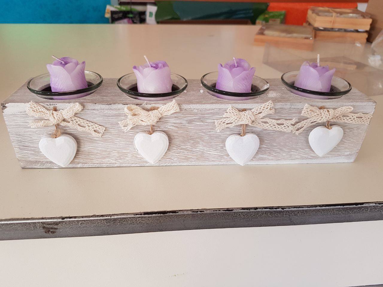 Portacandele con quattro candele color lavanda a forma di rosa, piattini in vetro, fiocchi in pizzo e cuori bianchi pendenti.