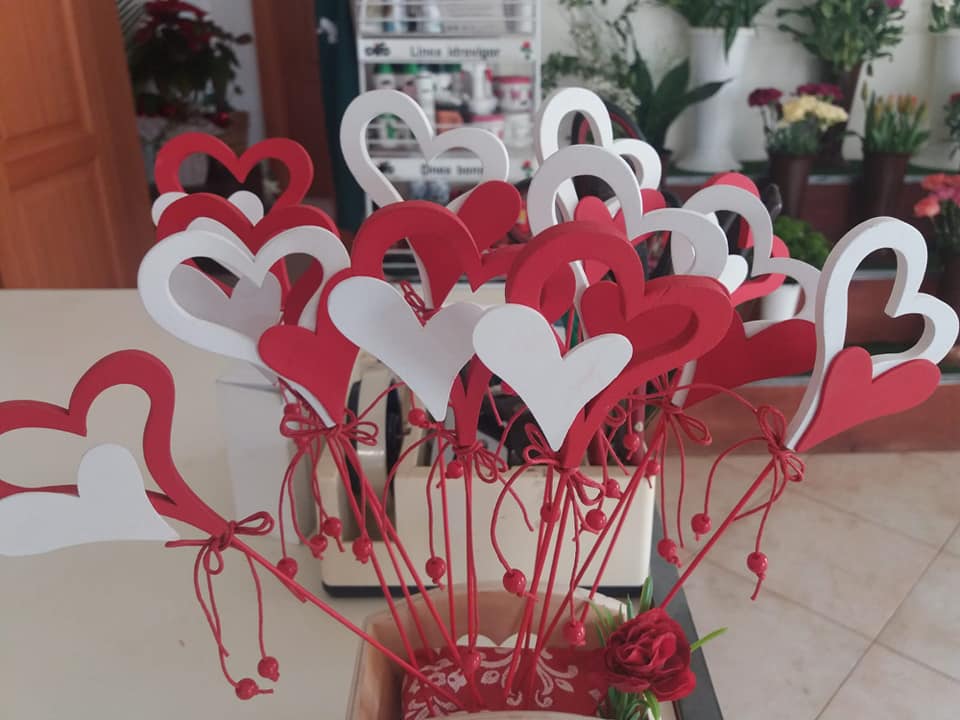 Composizione di decorazioni a forma di cuore rosse e bianche su bastoncini, legate con spago rosso in un vaso.